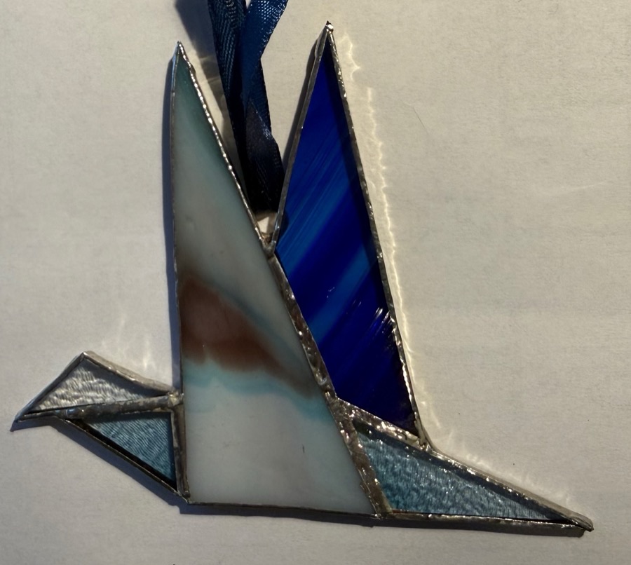 A small stained-glass bird in flight, its pieces of white, blue and pale blue glass joined by bright silver lines of solder.